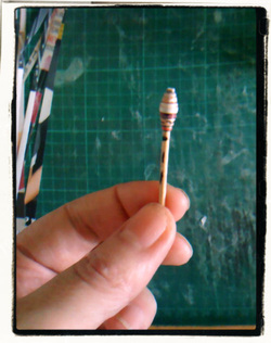 Handrolled paper bead on a stick.